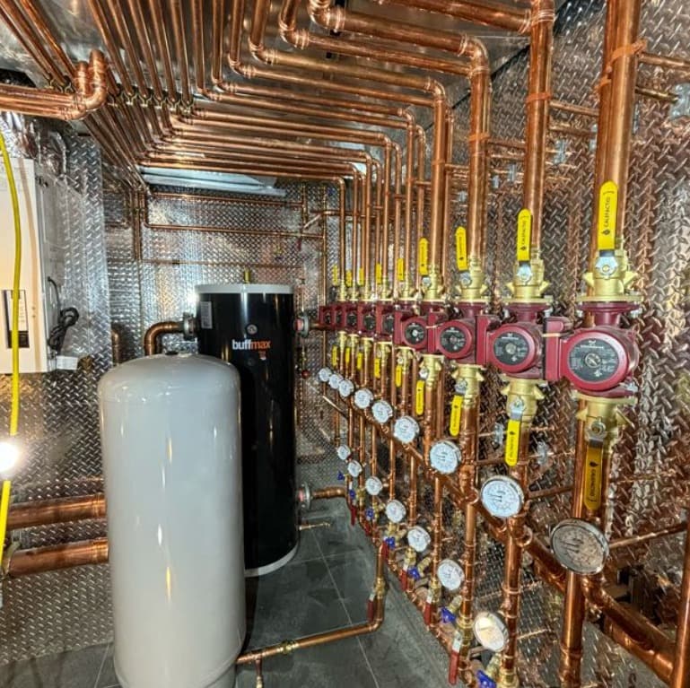 Hydronic mechanical room with copper piping, buffer tank, and zone manifolds